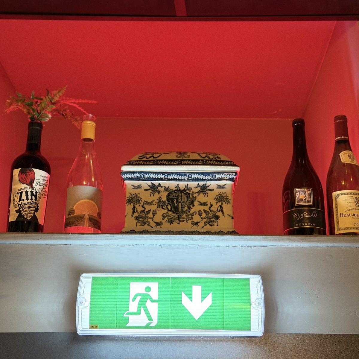 Maintained exit sign beneath a red-lit display niche of bottles
