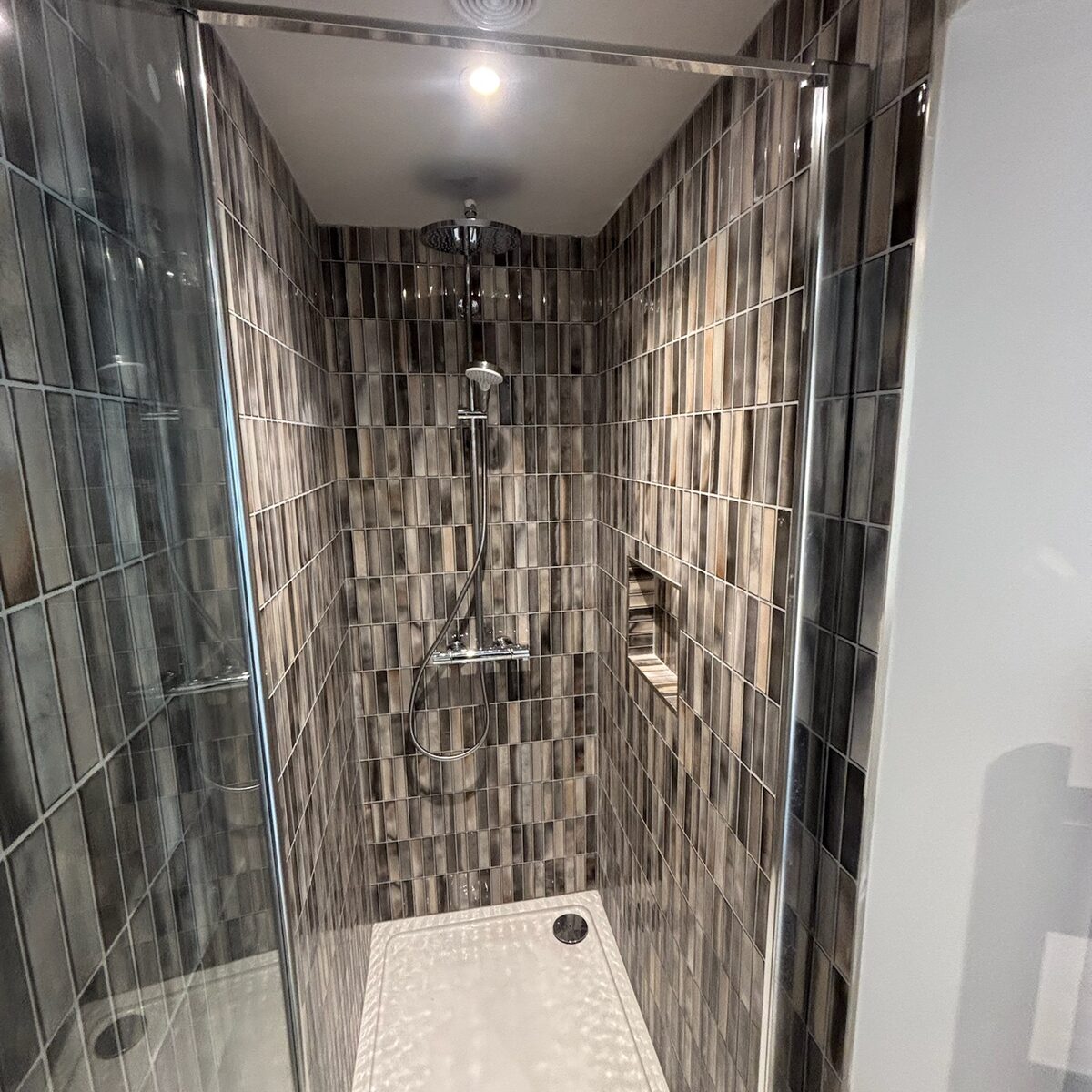 Shower room with dark tiling and lit niche